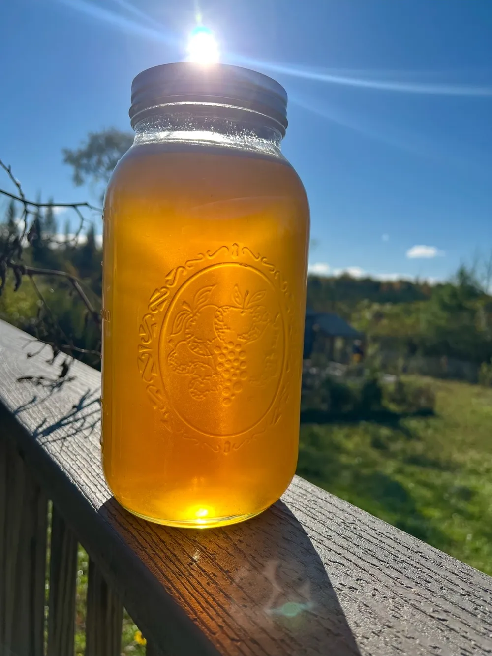 A jar of raw local honey glowing amber in the sun on a farmhouse porch rail
