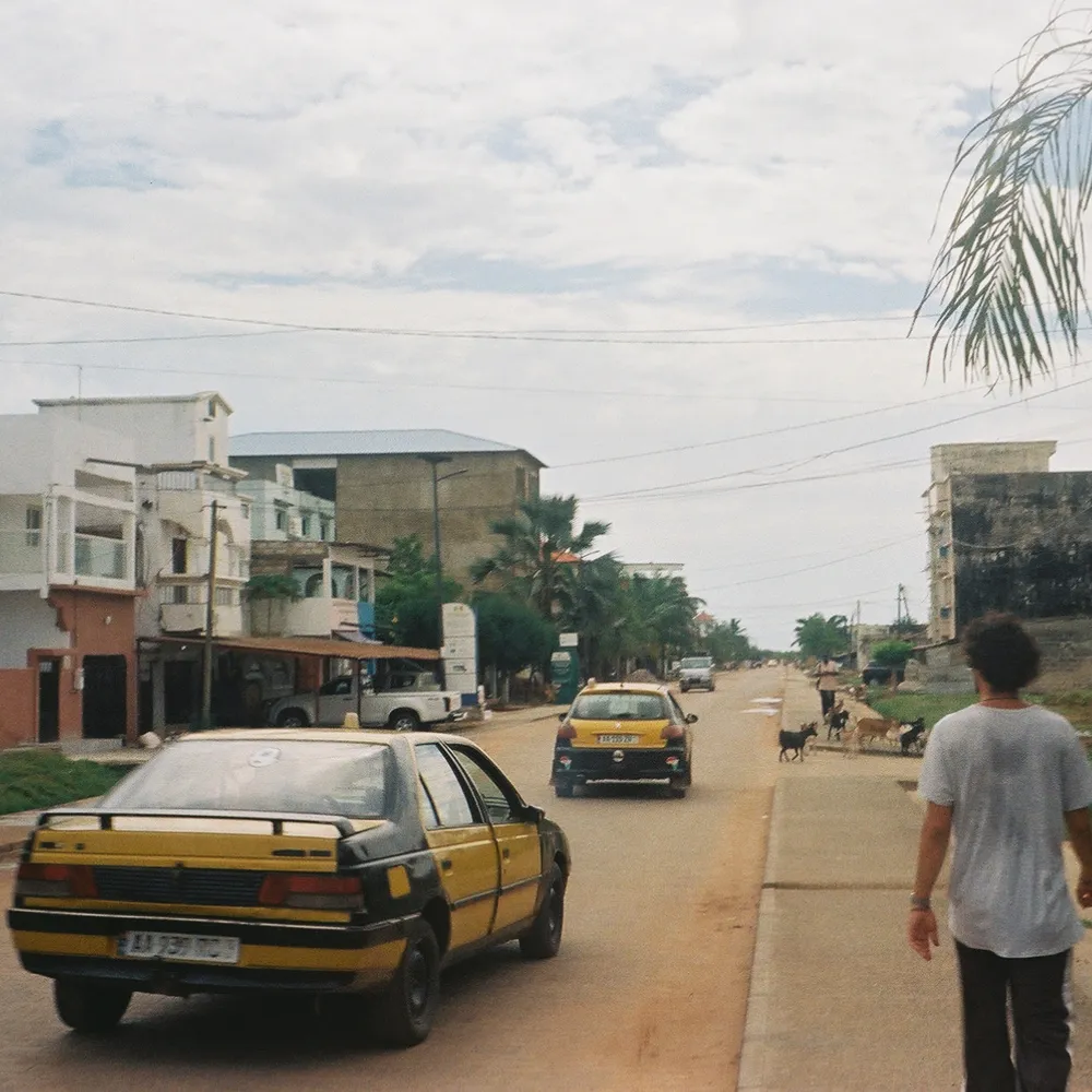 A street in Senegal with a yellow taxi and a man walking along the roadside